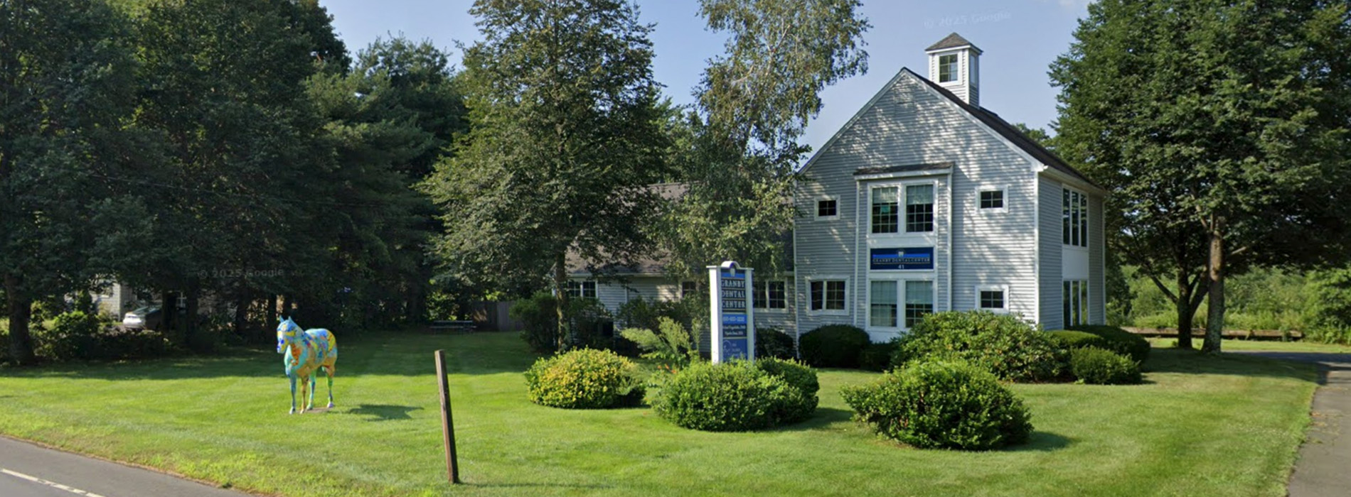 The image shows a single-story house with a white exterior and blue trim around the windows, situated in a suburban setting with trees and grass visible.