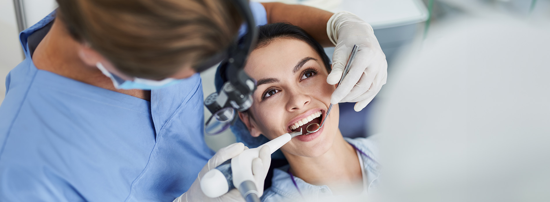 The image shows a dental professional performing oral surgery on a patient while wearing protective gear, with a focus on the dental equipment and the surgical setting.