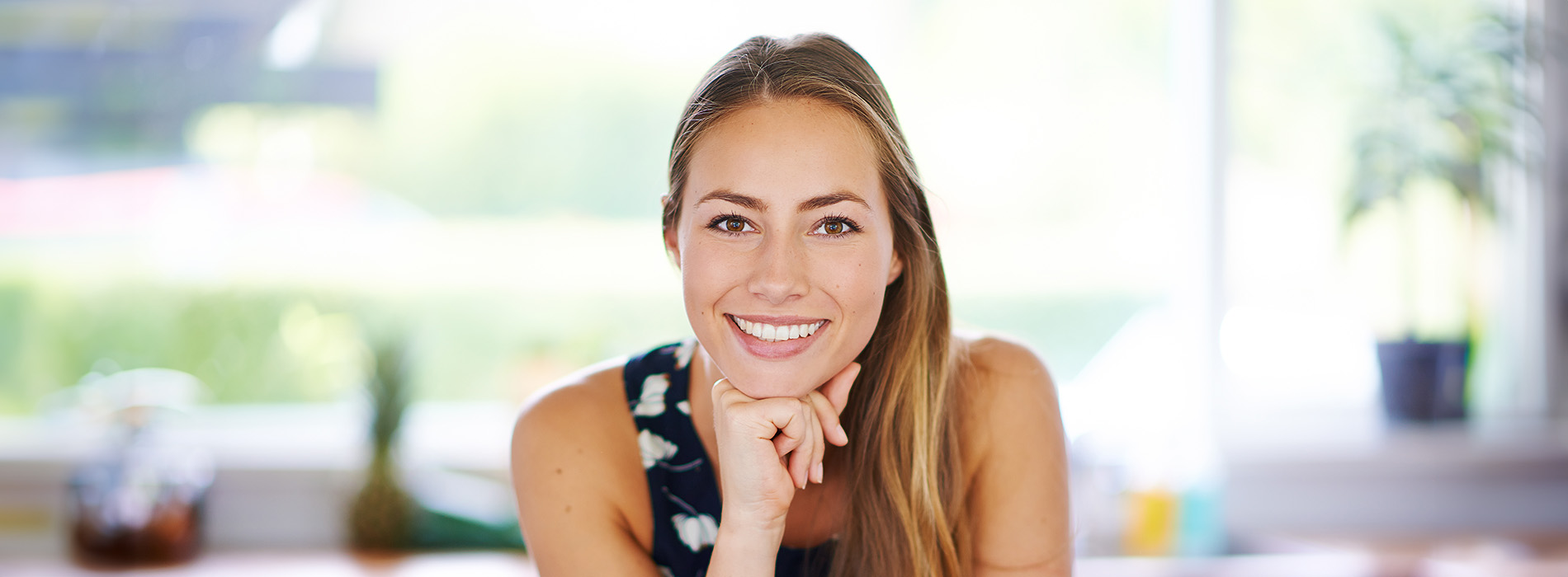 The image is a photograph of a woman with light skin, smiling at the camera. She appears to be in her late twenties or early thirties and has long hair. Her eyes are looking directly at the camera, and she is holding up her index finger near her mouth as if she s making a point or emphasizing something. The background is plain and light-colored, which suggests that this could be a stock photo used for various purposes such as advertising, personal branding, or lifestyle content.