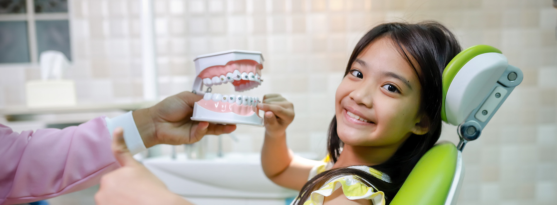 A young girl with a toothbrush in her mouth is being held up by an adult, possibly during a dental visit.