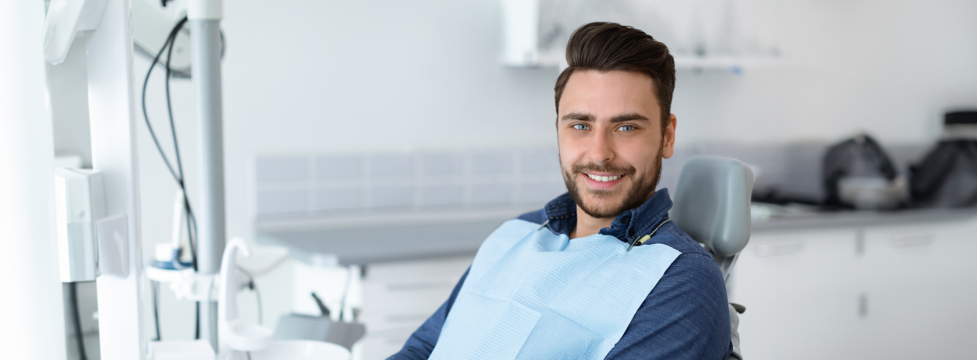 A person is seated in a dental chair, receiving care from a dental professional who stands behind them.