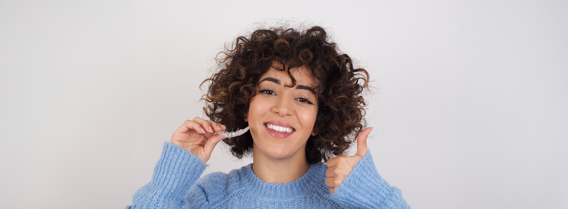 A woman with curly hair and a blue sweater smiling at the camera.