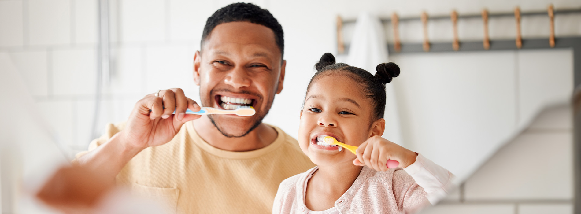 A man and a child brushing their teeth together in front of a bathroom mirror.