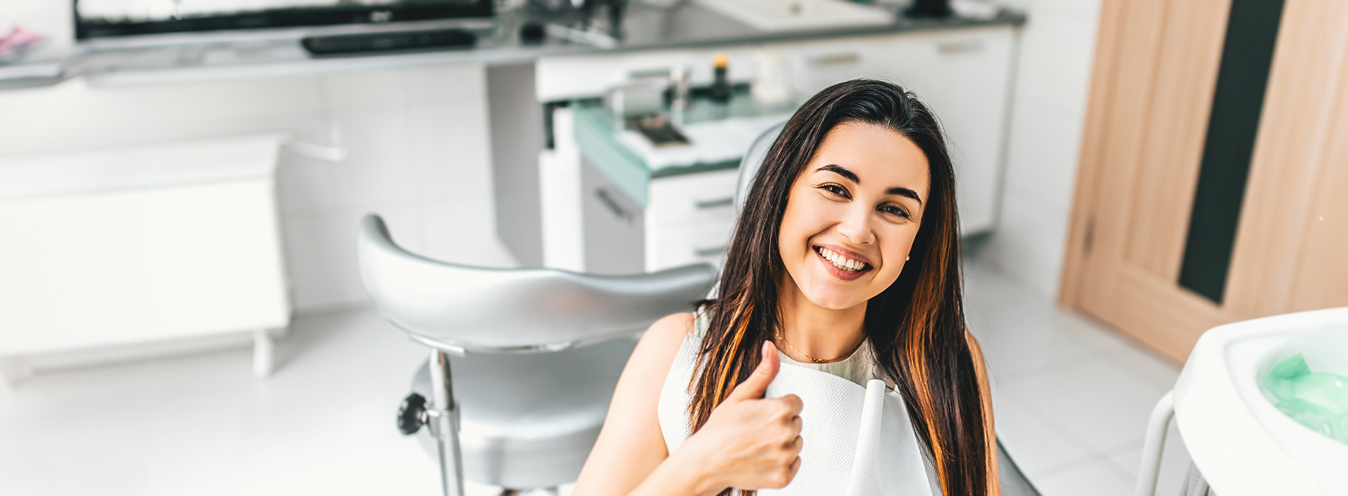 A woman sitting at a salon chair with a thumbs-up gesture, smiling towards the camera.