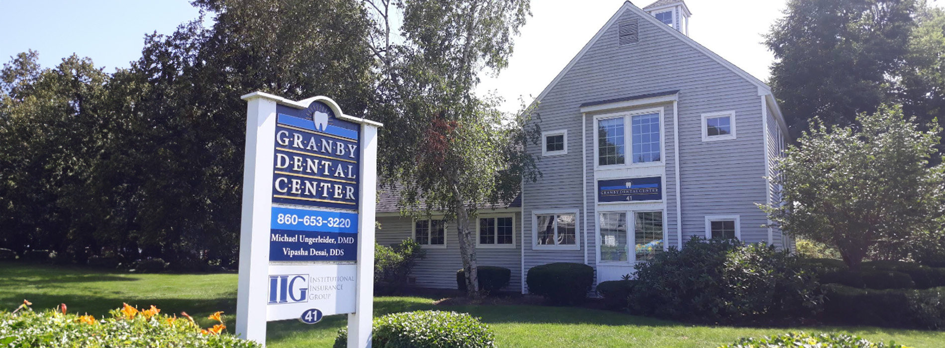 The image shows a real estate sign at the entrance of a building with a white exterior, set against a clear sky.