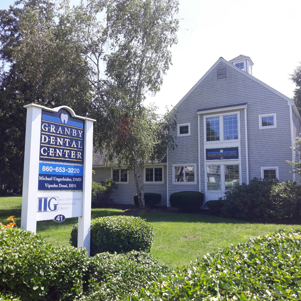 The image depicts a two-story dental practice building with a sign in front reading  Granby Dental Center  and a real estate sign indicating the property is for sale, set against a clear sky on a sunny day.