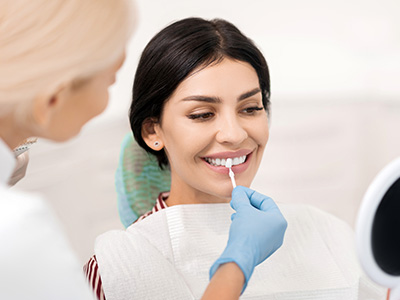 The image depicts a woman receiving dental care in a professional setting, with a dental hygienist performing a cleaning procedure while another person observes the process.