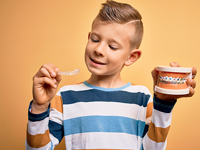 A young boy holding a toothbrush with a toothpaste tube in his other hand.