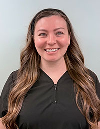 The image shows a woman with long hair wearing a professional black shirt, smiling at the camera, with her photo taken against a plain background.