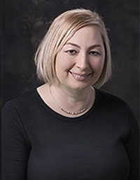 A woman with short hair, wearing glasses and a black top, smiling at the camera.