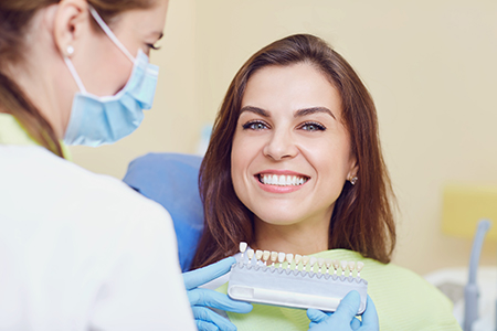 Woman receiving dental treatment, smiling at camera, with dental professional holding a dental device.