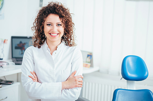 A woman with curly hair stands confidently in an office setting, smiling at the camera.
