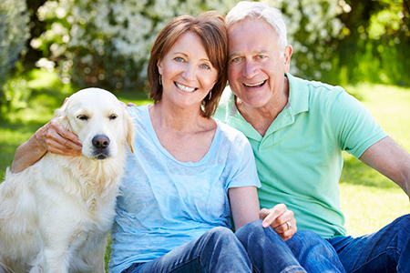 A man and woman are sitting outdoors with their golden retriever, smiling and posing for a photo together.