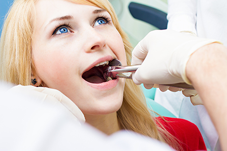 A woman receiving dental care from a professional with a focus on her open mouth and the dental instruments being used.