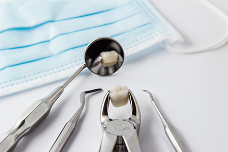 The image shows a collection of dental tools including a toothbrush with a toothpaste-covered bristle, a dental mirror, two pairs of tweezers, and a pair of scissors, all placed on a blue cloth, possibly in a dental office setting.