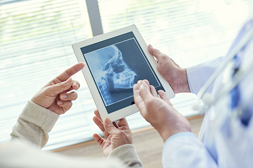 A tablet with an X-ray displayed on its screen being shown by two individuals in a medical setting.