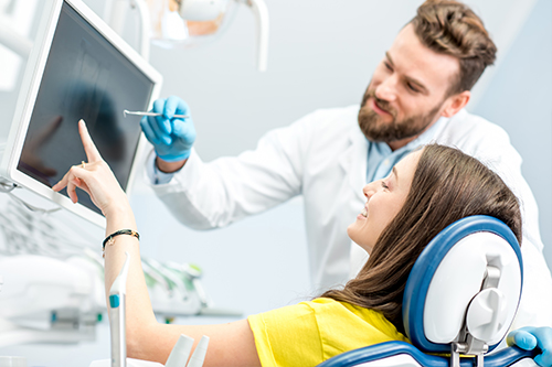 A man and woman are seated at a computer screen with medical equipment, possibly in a dental or healthcare setting.