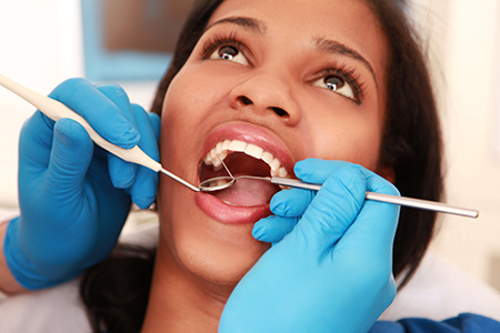 A woman receiving dental care with a dental hygienist using dental tools.