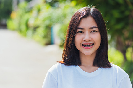 A young woman with short hair, smiling at the camera, wearing a white t-shirt, standing outdoors during daylight hours.