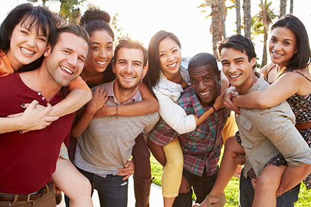A group of young adults posing together outdoors during daylight, smiling and embracing each other.