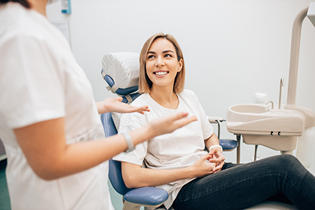 A woman sitting on a dental chair with a smile on her face, surrounded by dental professionals in a dental office setting.