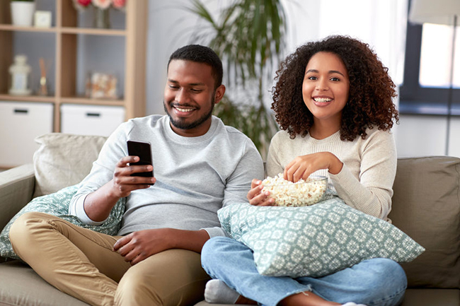 A young couple sitting on a couch, enjoying a movie together with popcorn.