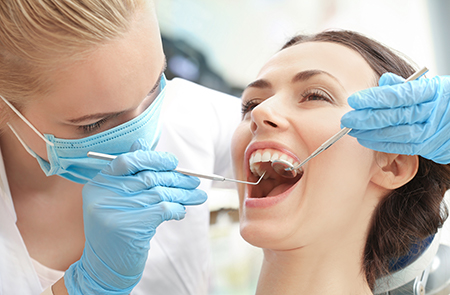 The image shows a dental hygienist performing a dental procedure on a patient s teeth using specialized equipment while wearing personal protective gear, with both individuals smiling at the camera.