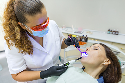 Woman dental hygienist using a dental laser on a patient s teeth.